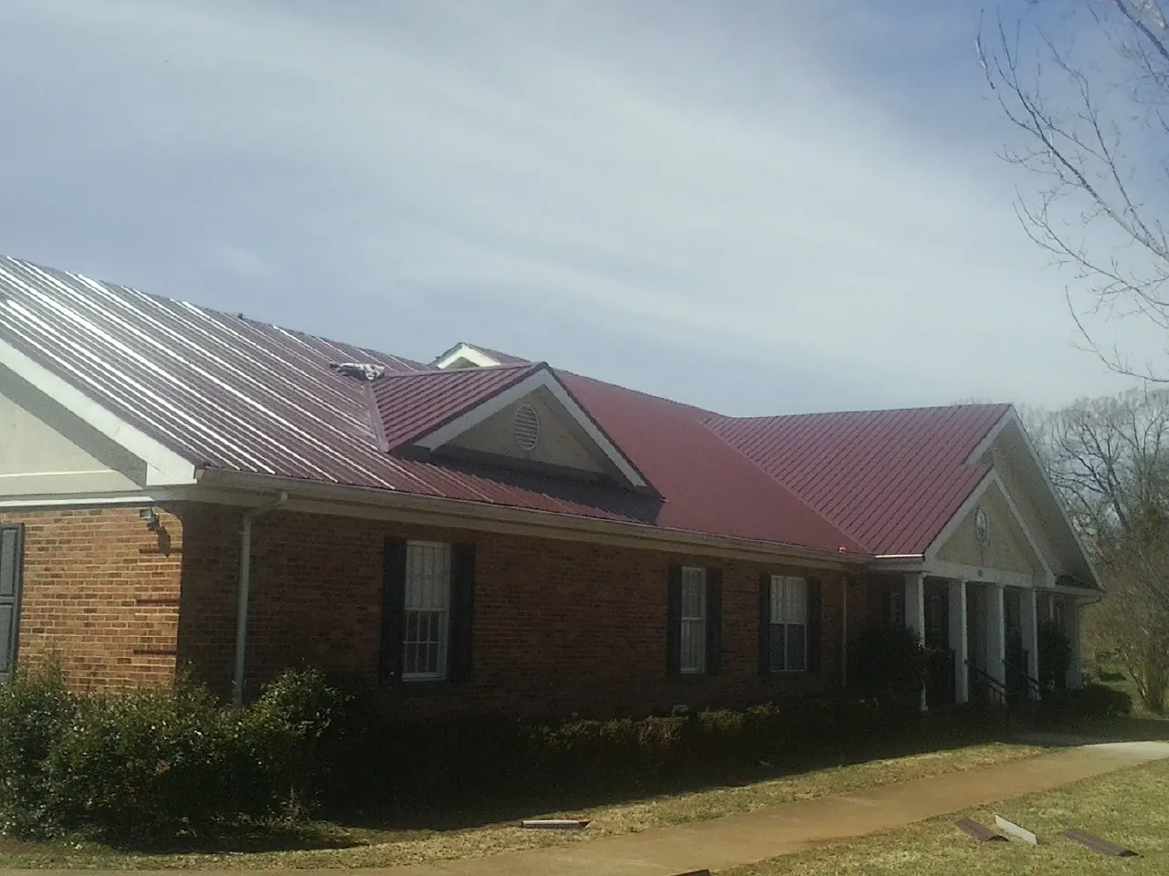 Red metal roof with gabled entries on a long brick building, from a Hail Damage Roof Repair job in Applegate