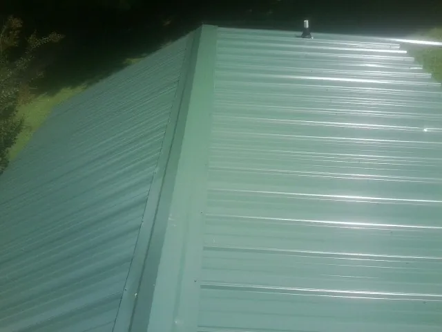New green metal panels meeting at the ridge of a roof — Flat Roof Repair work by our crew in Applegate